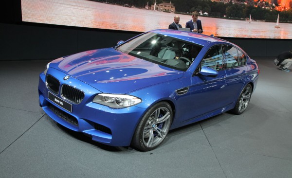Mavi BMW M5 sedan fuar standında ön sol üç çeyrek görünüm