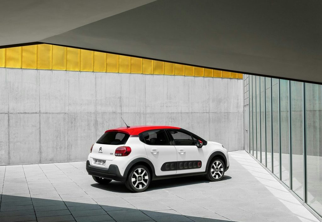 Citroen C3 beyaz gövde kırmızı tavan arka üç çeyrek mimari fonda