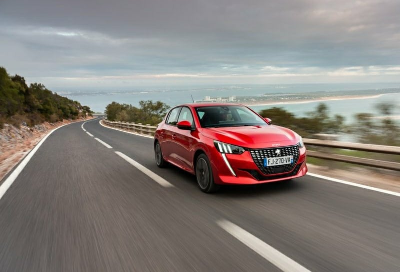 Virajlı kıyı yolunda ilerleyen kırmızı Peugeot 208