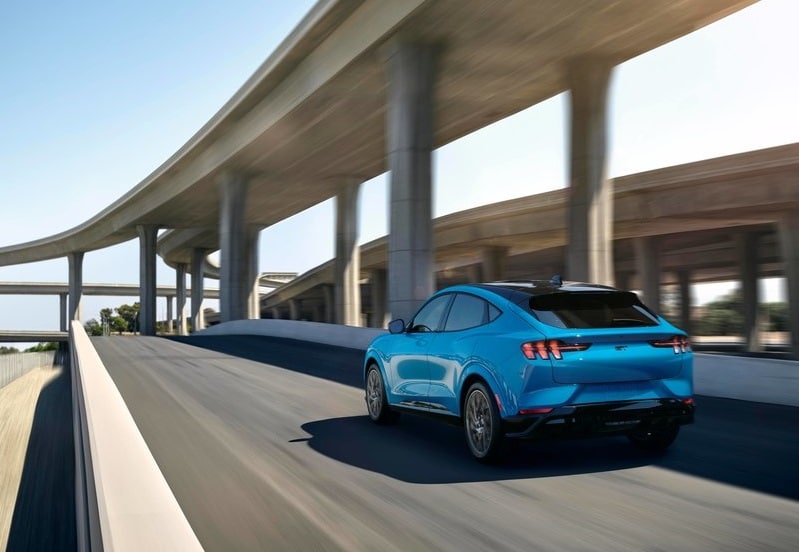 Mavi Mustang Mach-E yükseltilmiş şehir yolunda arkadan sürüş görünümü