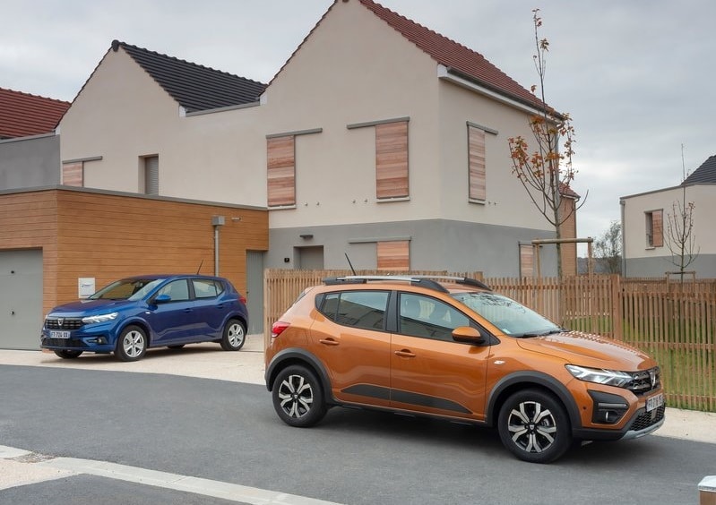 Konut önünde turuncu Dacia Sandero Stepway ve arka planda mavi otomobil