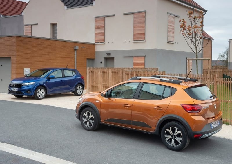Turuncu Dacia Sandero Stepway arka yan görünümü ve arka planda mavi otomobil