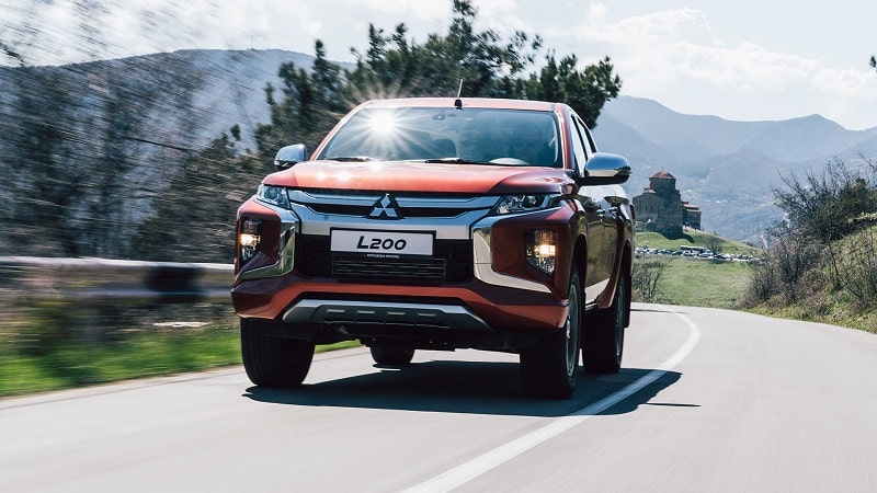 Turuncu Mitsubishi L200 virajlı yolda önden görünüm