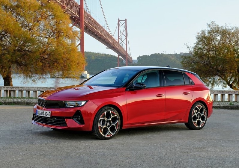 Kırmızı Opel Astra su kıyısında ön üç çeyrek görünümü