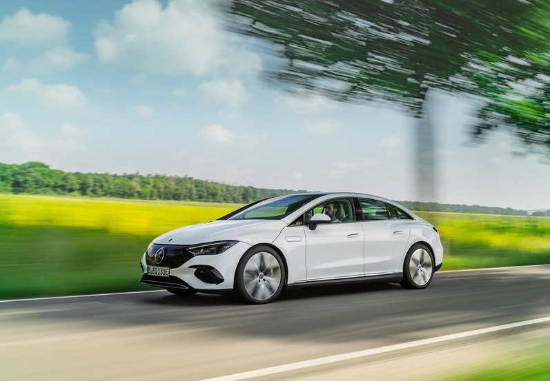 Beyaz Mercedes-Benz EQE sedanın açık yolda yan ve ön görünümü