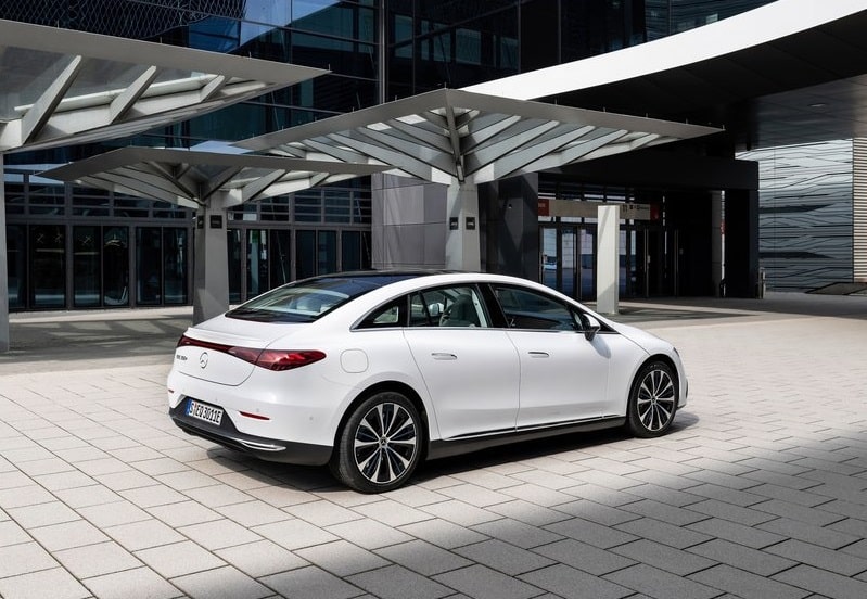 Beyaz Mercedes-Benz EQE sedanın modern bina önündeki arka üç çeyrek görünümü