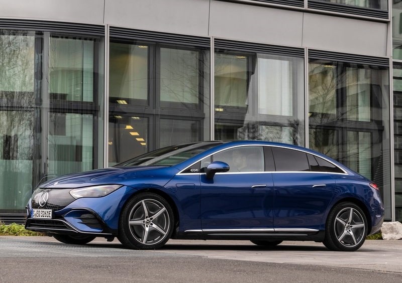 Mavi Mercedes-Benz EQE sedanın cam cepheli bina önünde park edilmiş görünümü