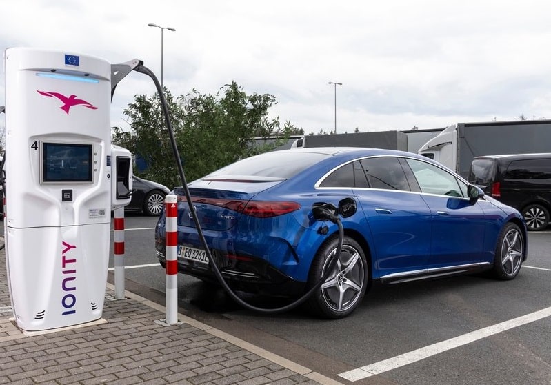 Mavi Mercedes-Benz EQE sedanın hızlı şarj istasyonuna bağlı arka görünümü