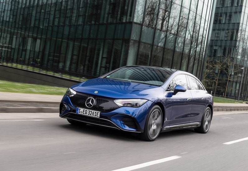 Mavi Mercedes-Benz EQE sedanın şehir içinde önden üç çeyrek hareket görüntüsü