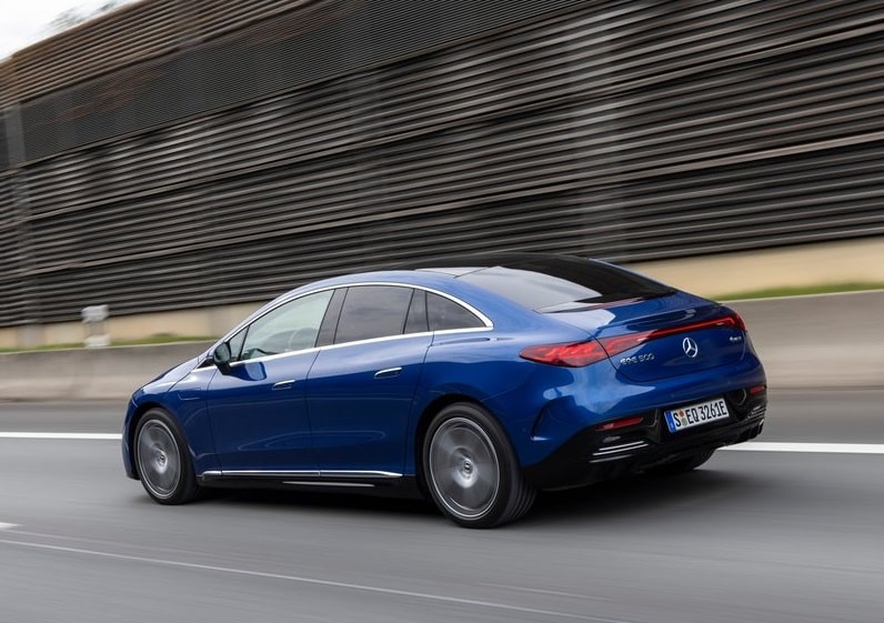 Mavi Mercedes-Benz EQE sedanın yolda hareket halindeki arka üç çeyrek görünümü