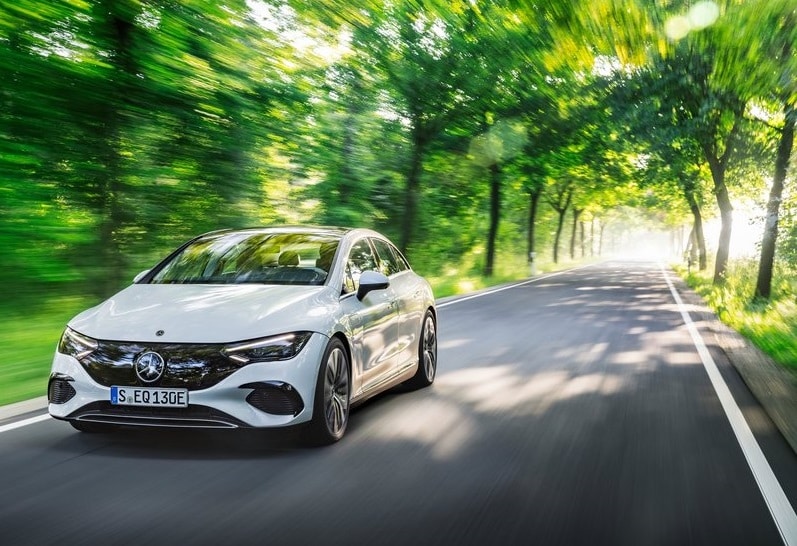 Beyaz Mercedes-Benz EQE sedanın ağaçlıklı yolda hareket halindeki görünümü