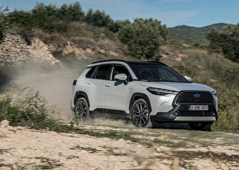 Beyaz Toyota Corolla Cross modelinin toprak zeminde hareket halindeki görünümü